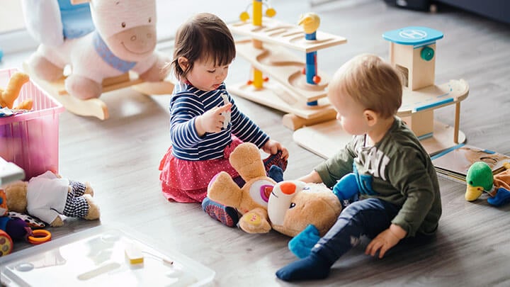 Dos niños juntos en el suelo rodeados de juguetes y peluches.