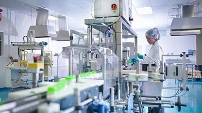 Trabajador inspeccionando productos en la línea de producción en una fábrica farmacéutica.